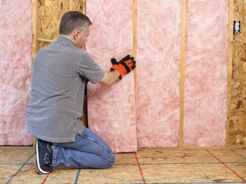 Man installing fiberglass insulation in the wall of an attic.
